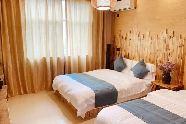 A hotel room with two beds, beige curtains, a wooden headboard, and a bedside table with a vase.
