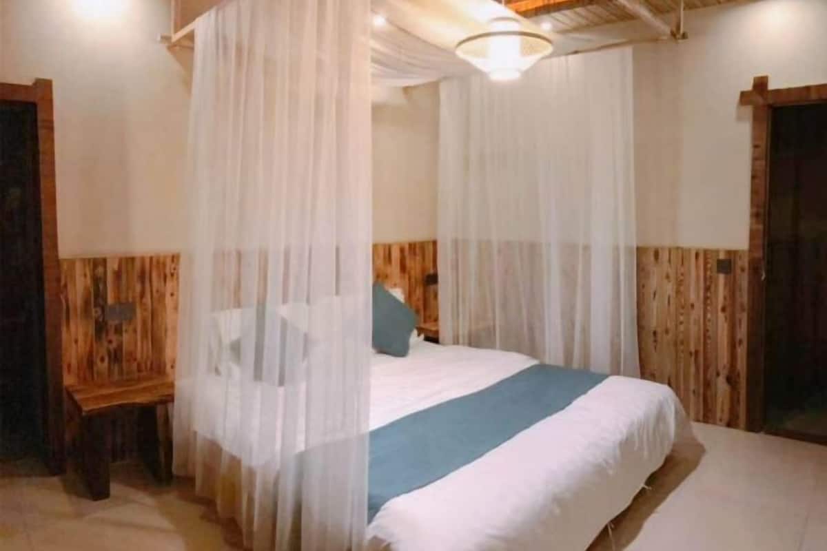 A room with a bed under a canopy, wooden walls, a small wooden table, and a ceiling light.