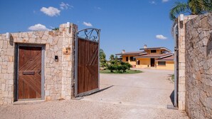 Une entrée fermée par un portail, avec des murs en pierre et un portail en métal, qui mène à une maison dotée d’un toit en tuiles et d’une pelouse bien entretenue.