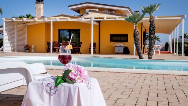 Une vue sur la piscine, avec une table, des chaises et un verre de vin rouge.