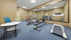Ein Fitnessraum mit Trainingsgeräten, Laufband und Tisch mit Stuhl.