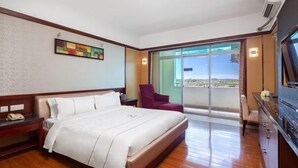 A hotel room with a bed, a desk with a telephone, a chair, a TV, and a balcony with a view. - Fenghuangcheng Hotel (Wenchang)