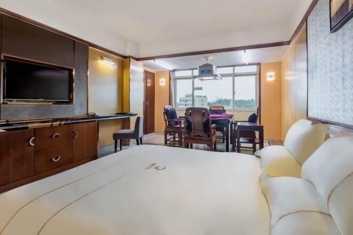 Habitación de hotel con cama, televisión, escritorio con sillas y ventana con vistas.