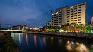 A multi-story hotel with a modern design, located beside a calm body of water, reflecting the building and surrounding lights. - Fenghuangcheng Hotel (Wenchang)