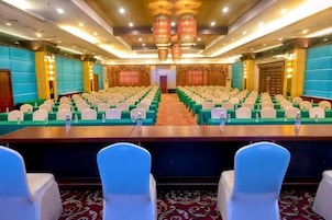 Un salón de conferencias con filas de sillas, una mesa larga y un escenario al frente.