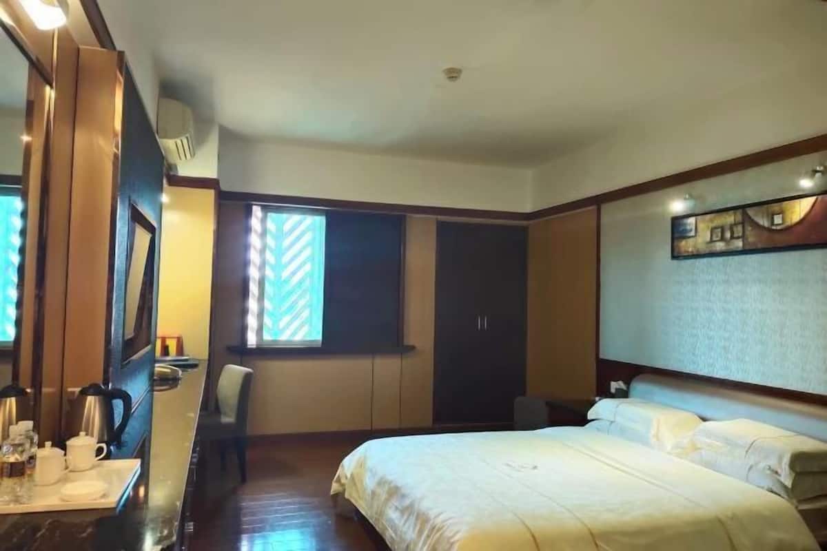 Habitación de hotel con cama, escritorio con cafetera, silla, armario y ventana con persianas.