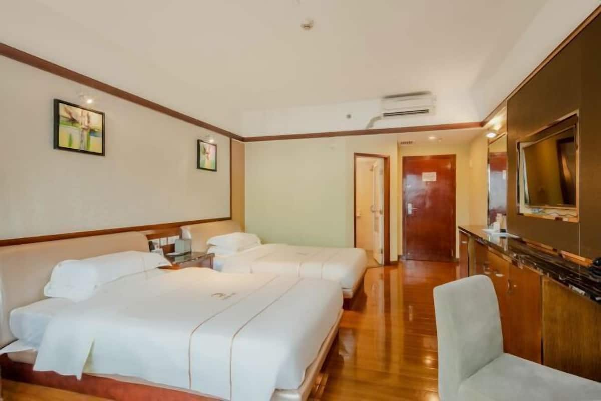 Habitación de hotel con una cama grande, una cama más pequeña, un escritorio con una silla, un televisor y piso de madera.