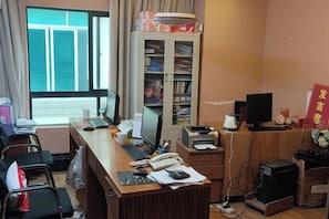 Una camera d'albergo con una scrivania, computer, telefono e una libreria.