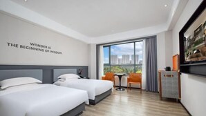 A hotel room with two beds, a desk, a chair, a small table, and a large window with a view of buildings. - Fenghuangcheng Hotel (Wenchang)