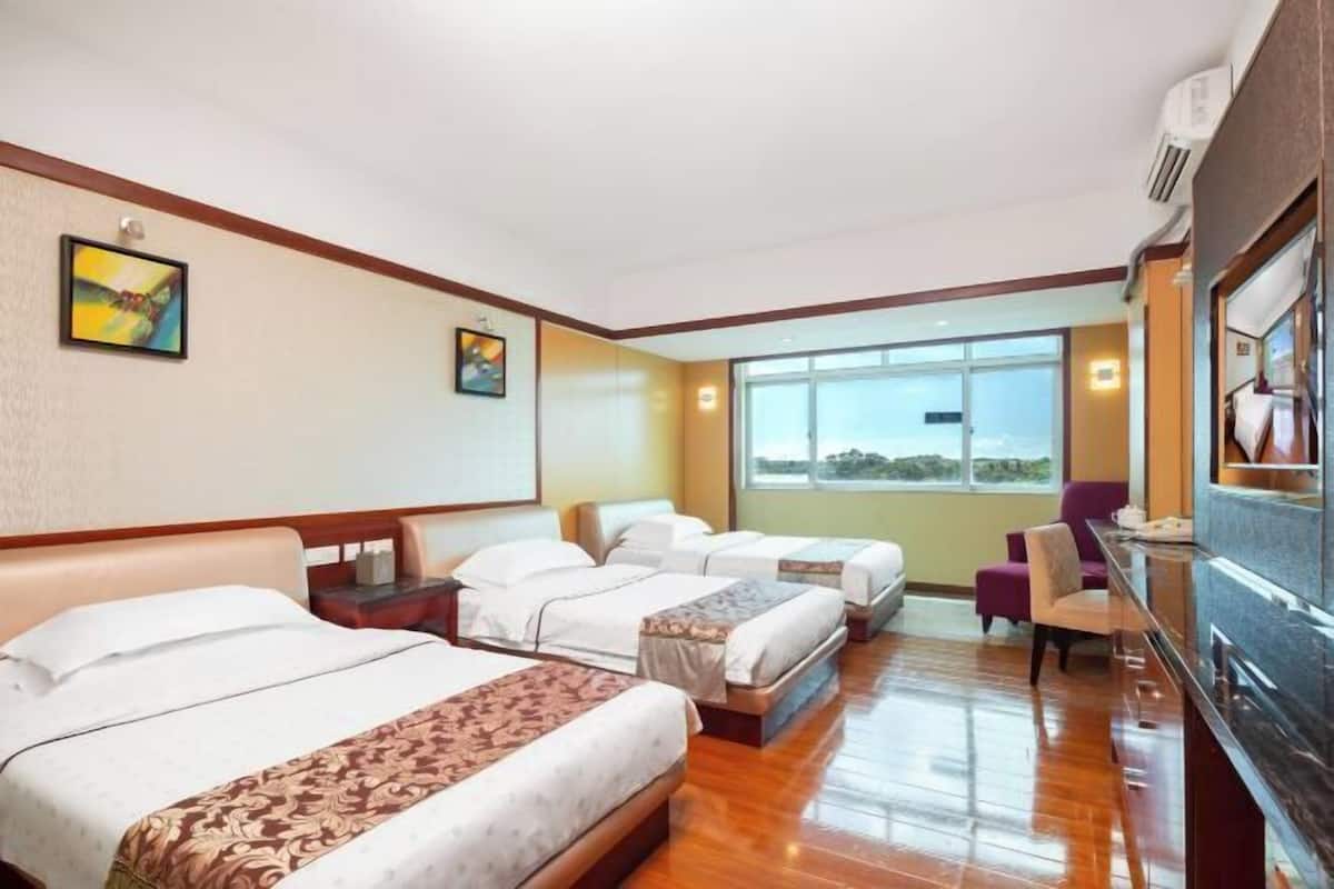 Una habitación de hotel con tres camas, un televisor y un ventanal grande.
