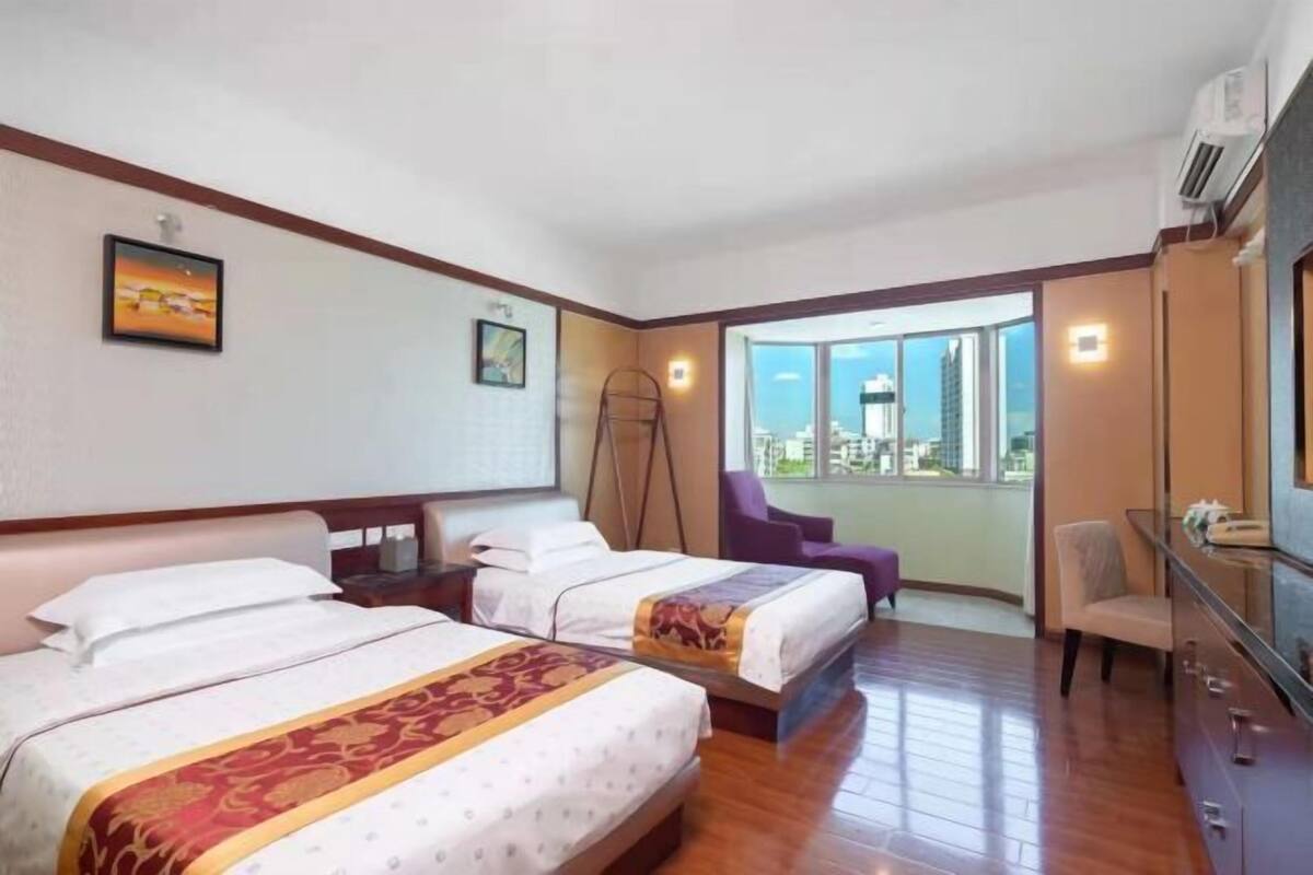 Habitación de hotel con dos camas, un escritorio, una silla y vista a la ciudad.
