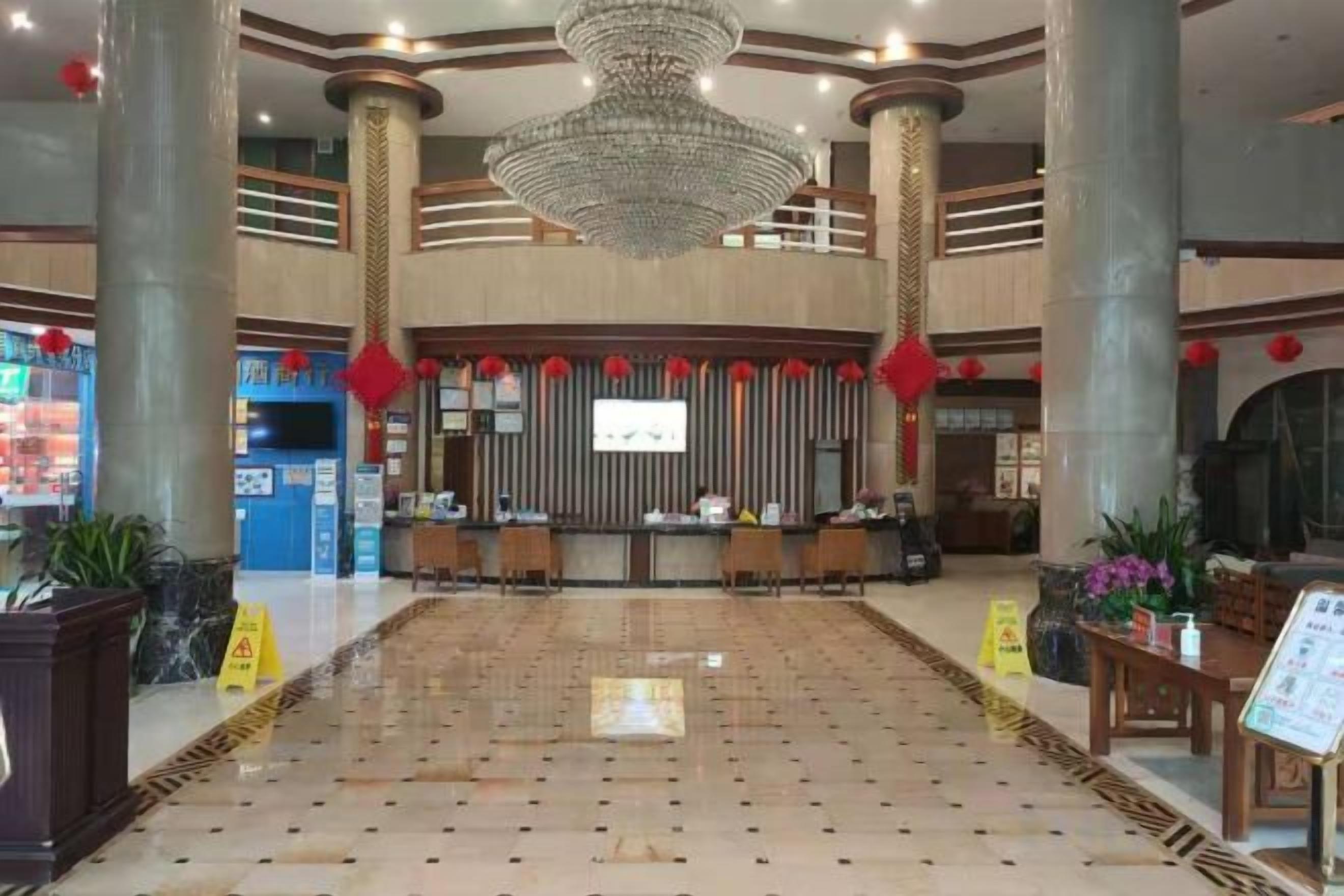 Um lobby amplo com balcão de recepção, colunas imponentes e um lustre.