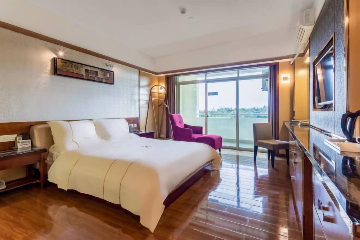 Habitación de hotel con una cama grande, un escritorio con silla, televisión y balcón con vistas.