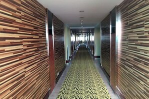 A corridor with patterned walls and a patterned carpet, leading to a bright area at the end. - Fenghuangcheng Hotel (Wenchang)