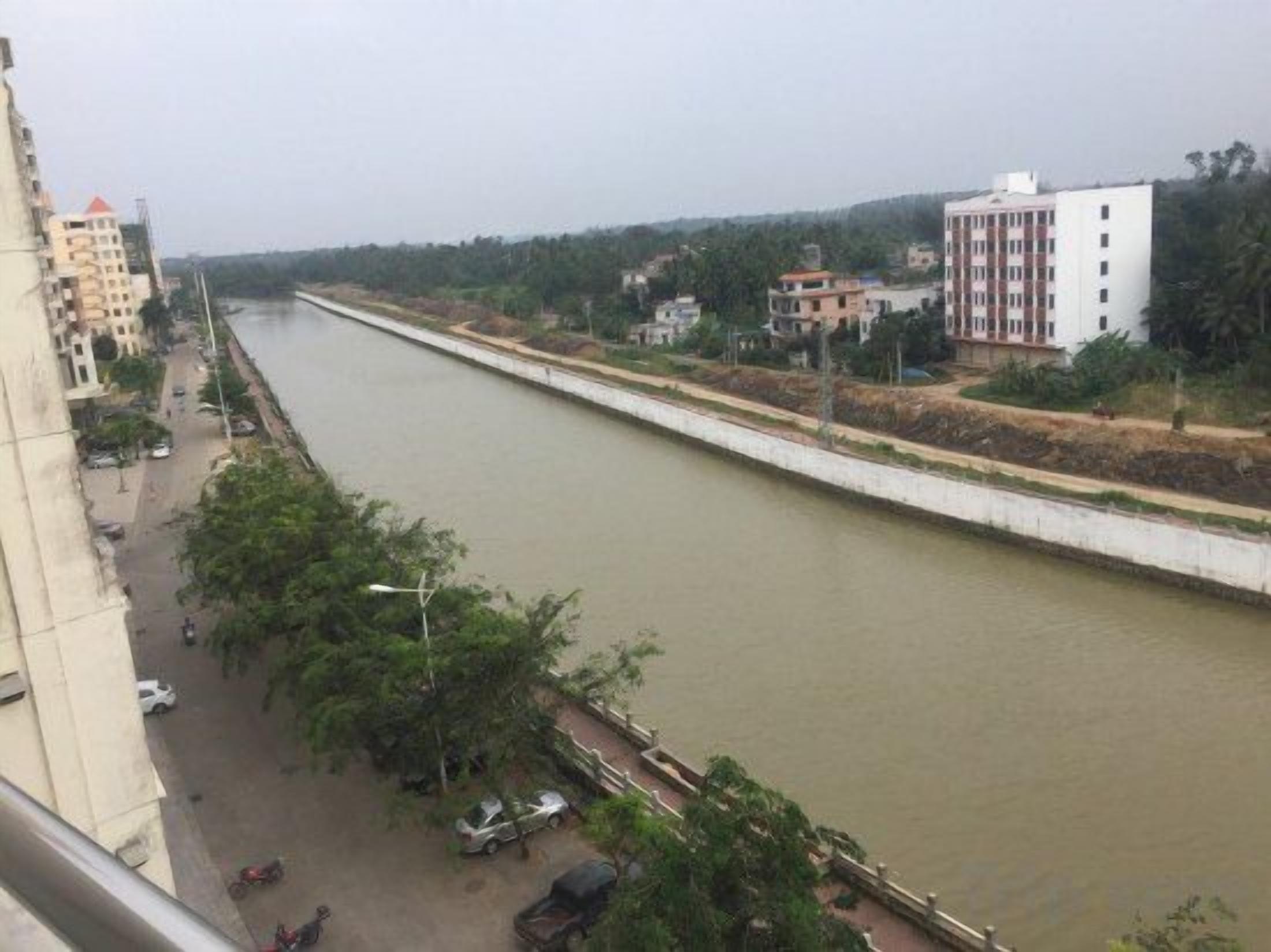 A river running alongside a road with buildings on one side.