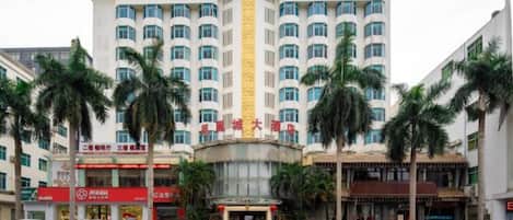 Un hotel de varios pisos con fachada curva, palmeras en primer plano y varios automóviles estacionados.