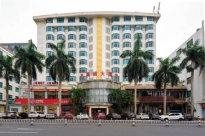 A multi-story hotel with a curved facade, palm trees in front, and several cars parked in front. - Fenghuangcheng Hotel (Wenchang)