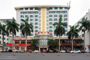 Un hotel de varios pisos con fachada curva, palmeras en primer plano y varios automóviles estacionados.