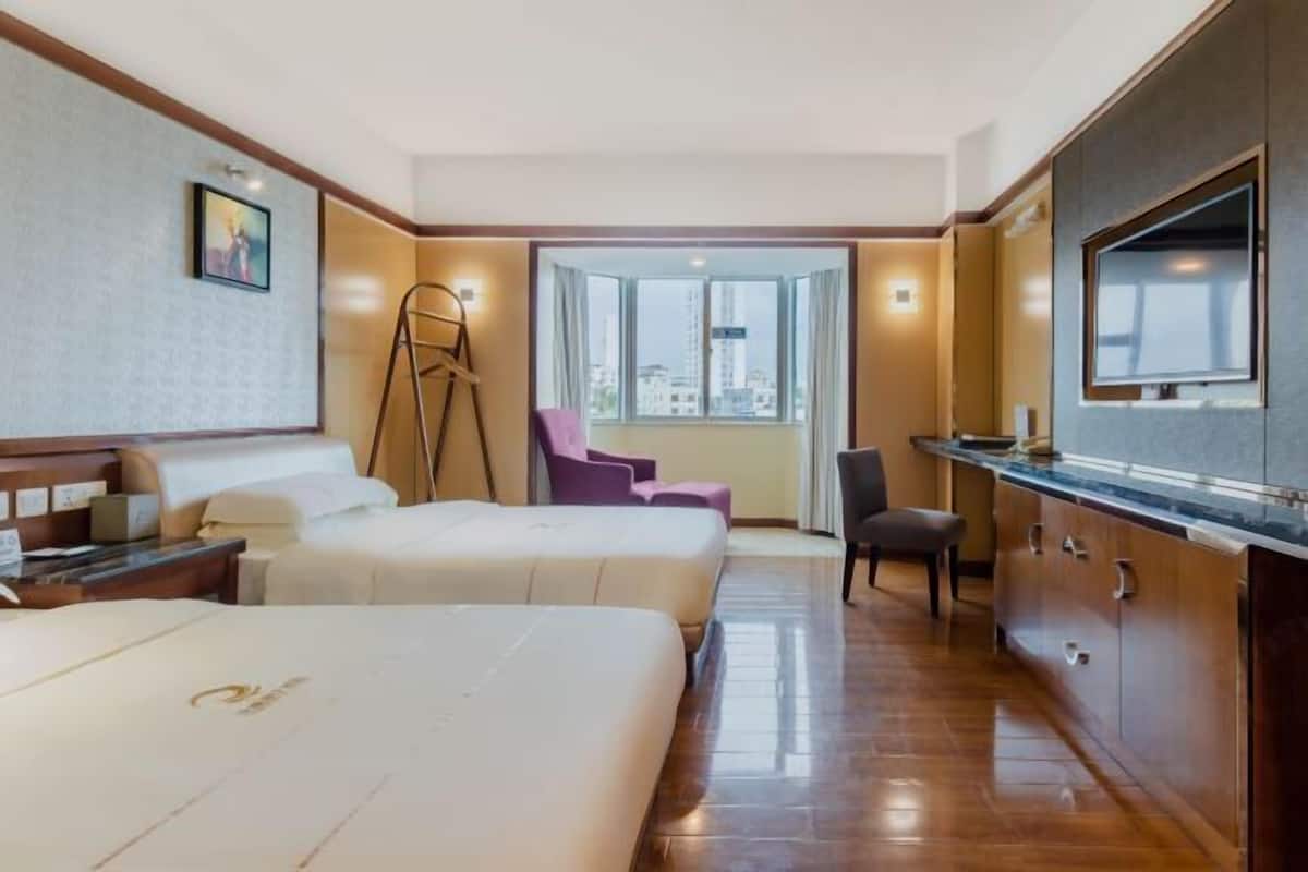 Habitación de hotel con dos camas, un escritorio, una silla, un televisor y un ventanal con vistas a edificios.
