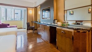 A modern hotel room with a wooden floor, a large window with a city view, a kitchenette, and a bed with a purple accent. - Fenghuangcheng Hotel (Wenchang)
