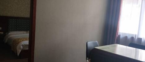 A hotel room with a bed, a wooden table, a chair, and a trash bin.