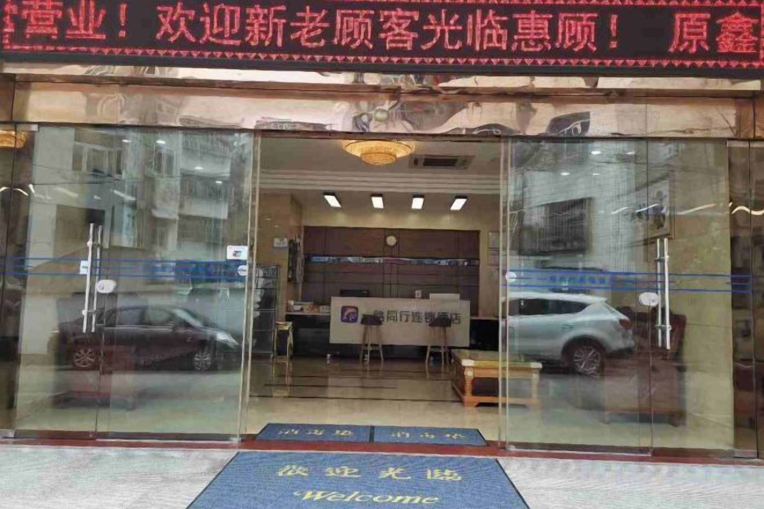 A hotel entrance with a reception desk, a car parked outside, and a welcome mat.