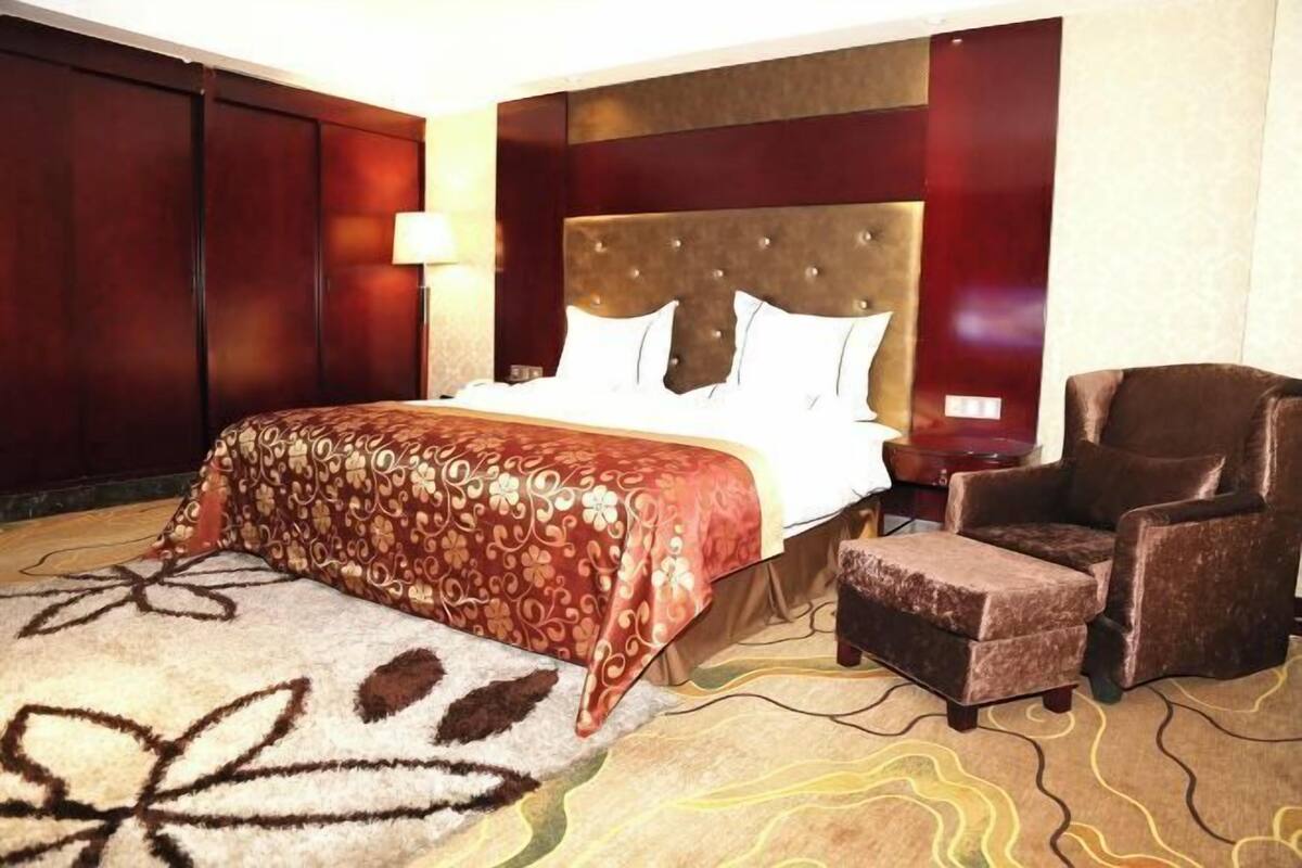 Une chambre d’hôtel avec un grand lit, une chaise, une table de chevet et une lampe.