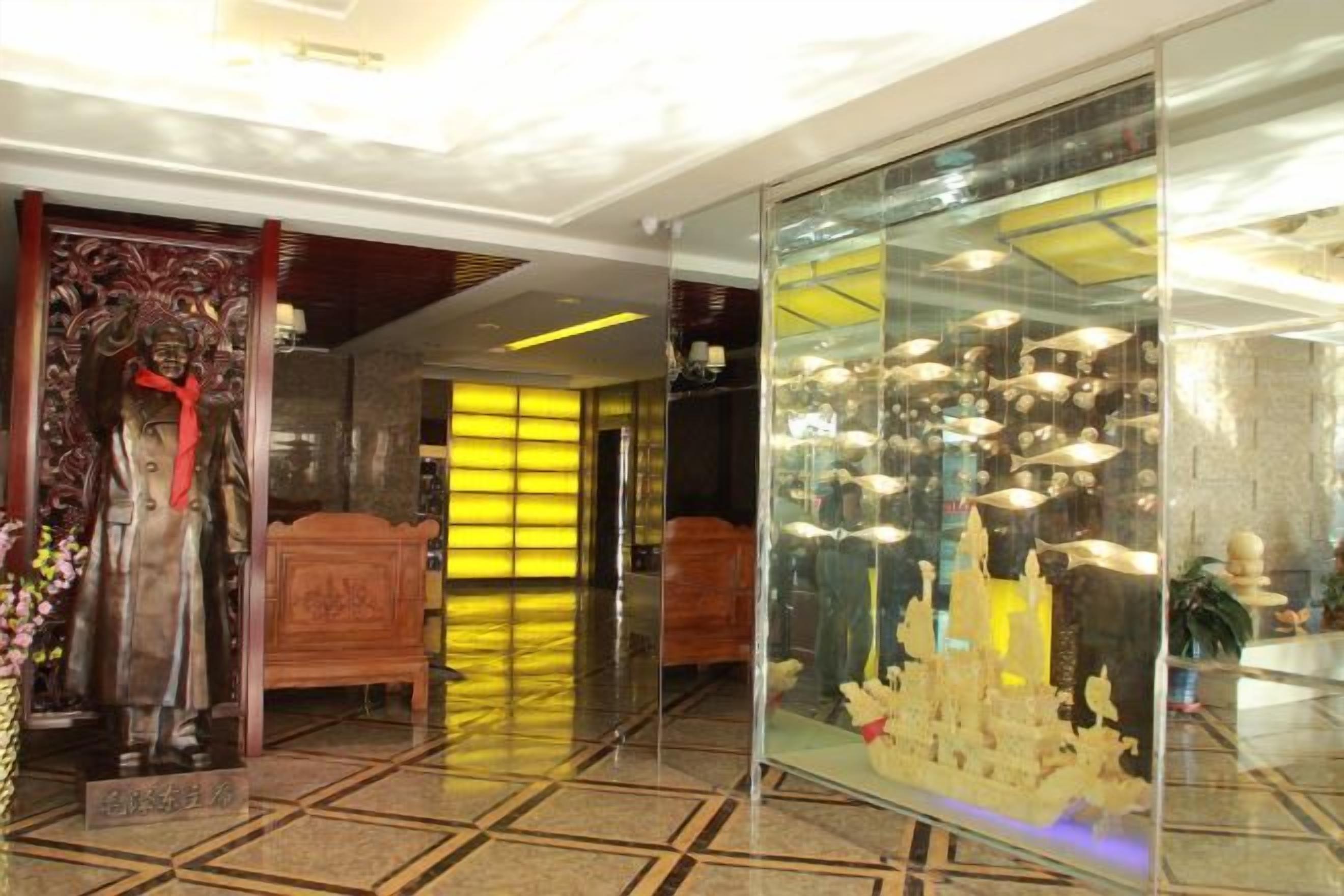 A hotel lobby with a statue, a glass display case with items, and a bed in the background.