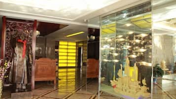 A hotel lobby with a statue, a glass display case with items, and a bed in the background.