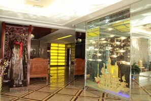 Un vestíbulo de hotel con una estatua, una vitrina con objetos y una cama al fondo.