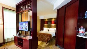 Habitación de hotel con televisor, cama con colcha estampada, armario de madera y alfombra de diseño geométrico.