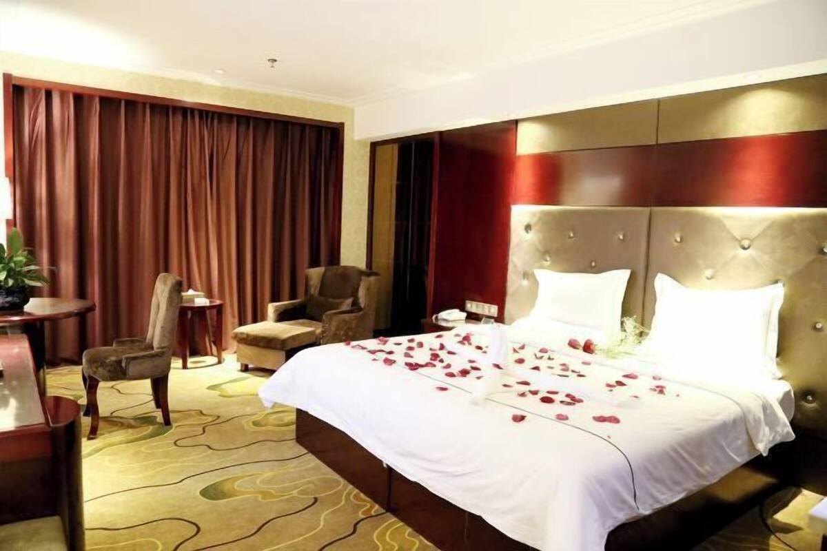 Une chambre d’hôtel avec un grand lit, une tête de lit, un bureau, une chaise et un rideau.