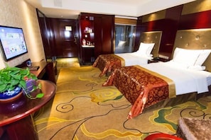 Una habitación de hotel con dos camas, televisión, escritorio con planta y alfombra estampada.