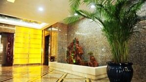 Un hall con piso de mármol, mostrador de recepción, planta en maceta y un elemento decorativo en la pared.