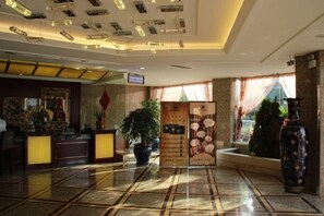A hotel lobby with a reception desk, a large potted plant, a decorative vase, and a tiled floor. - Haijingtian Business Hotel (Wu Weiletai Shop) (Wuwei)