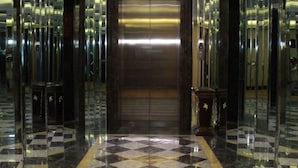 Un vestíbulo elegante con suelo a cuadros y paredes espejadas, que conduce a un ascensor.