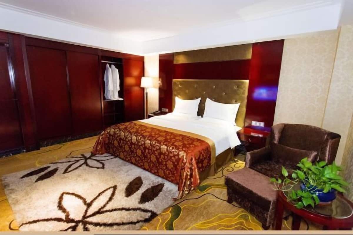 Une chambre d’hôtel avec un grand lit, une chaise, une petite table avec une plante et une armoire.