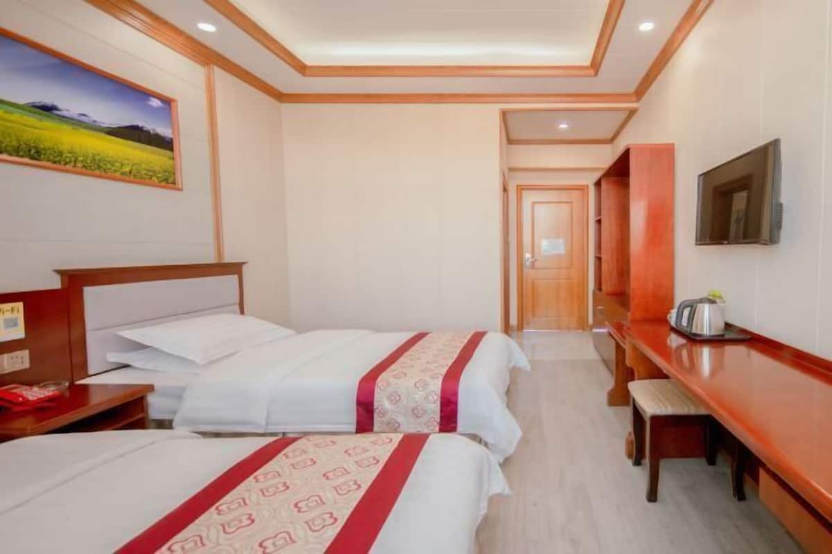 A hotel room with two beds, a wooden desk, a television, and a painting on the wall.