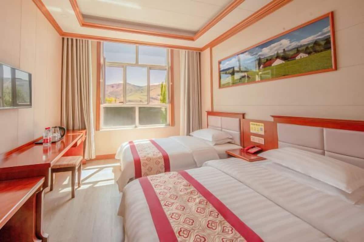 A hotel room with two beds, a desk, a chair, a window with curtains, and a painting on the wall.