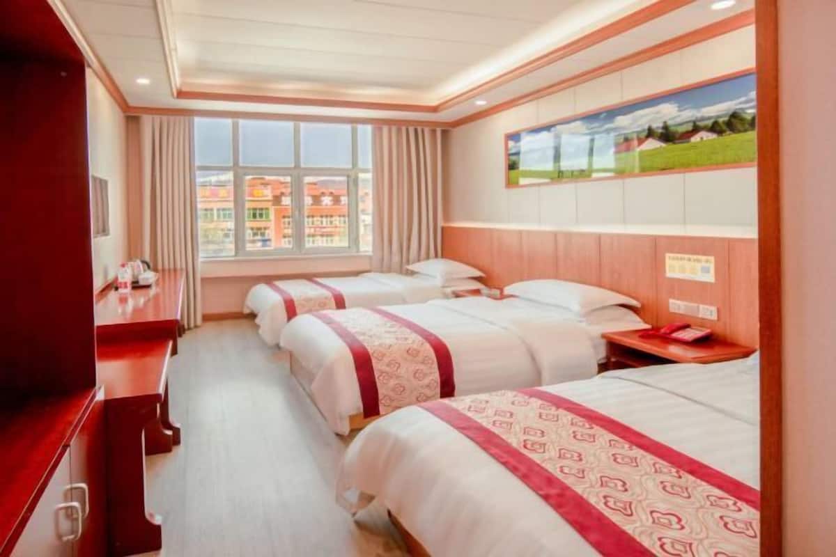A hotel room with two beds, a desk, a window with curtains, and a painting on the wall.