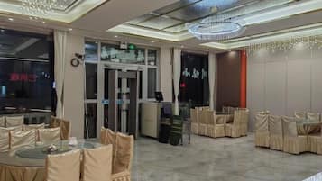 A hotel lobby with round tables, chairs, a revolving door, and a chandelier.