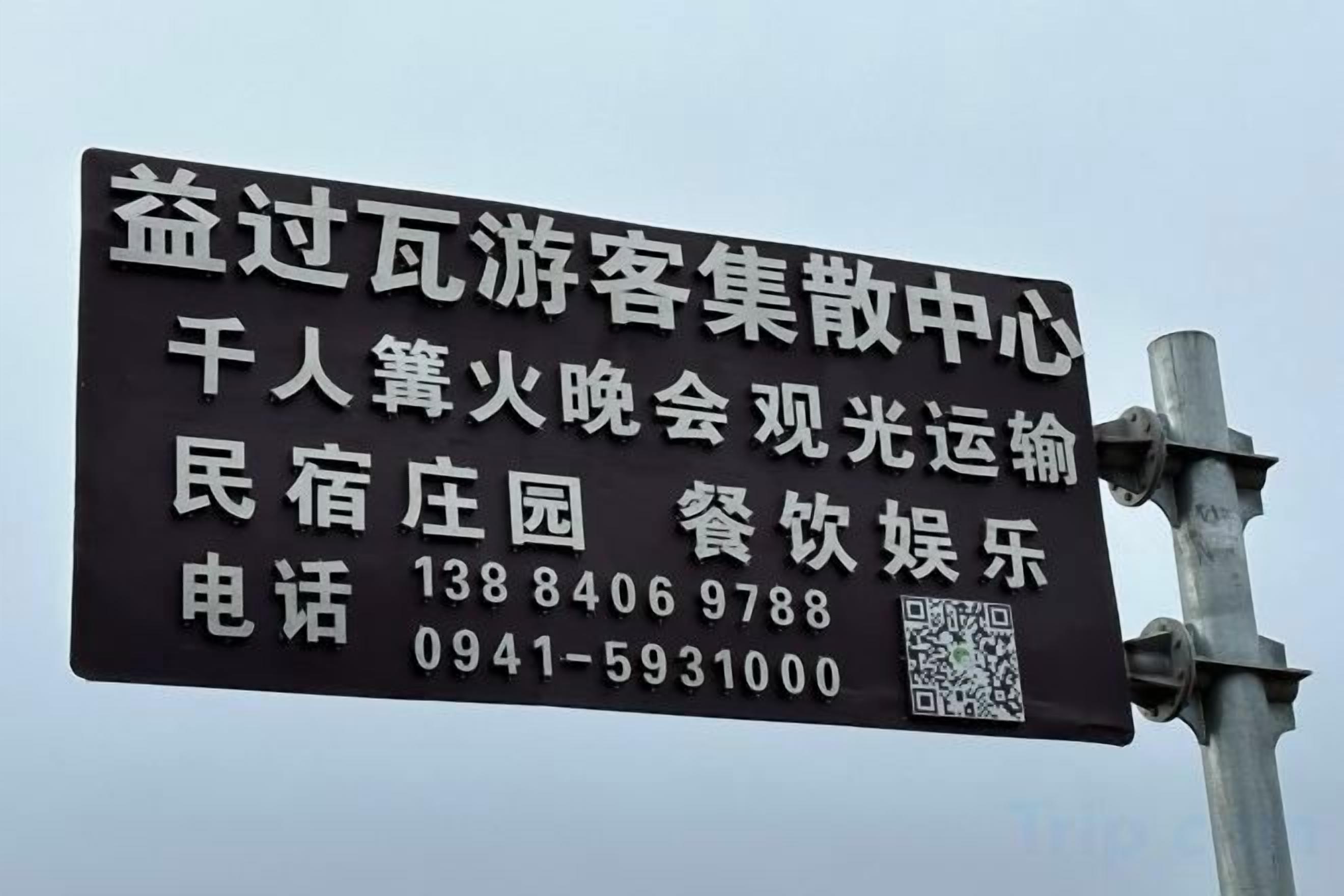 Un panneau avec du texte et un code QR, fixé sur un poteau métallique.