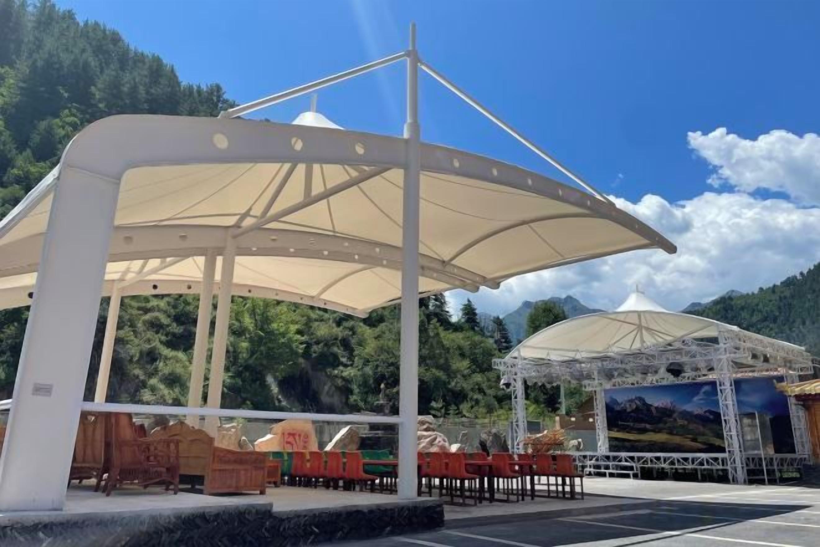 A covered outdoor seating area with tables and chairs, a stage, and a backdrop with a landscape painting.