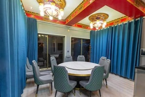 Une salle de conférence avec une table ronde et des chaises, des rideaux bleus et un lustre.