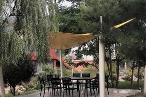 Un'area pranzo all'aperto con tavolo e sedie, circondata da alberi e un edificio sullo sfondo.