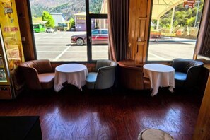 A seating area with two round tables and four chairs, a wooden floor, and a view of a parking lot through large windows.