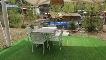 Un área de comedor al aire libre cubierta con una mesa y sillas, rodeada de follaje y una piscina.