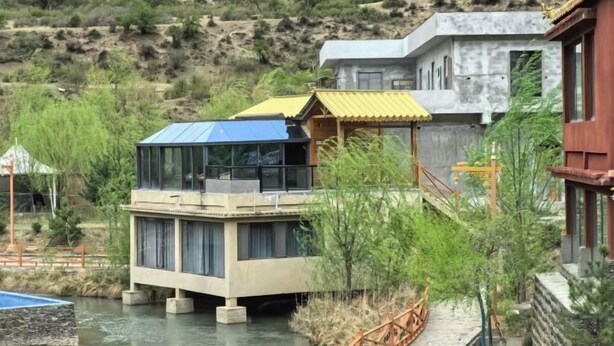 Un edificio moderno con cerramiento de vidrio, una terraza de madera y un cuerpo de agua.
