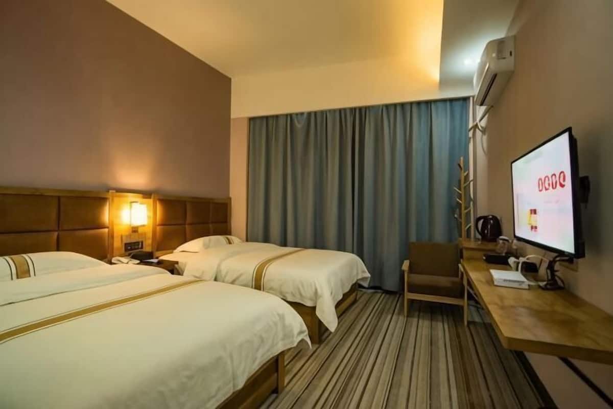 A hotel room with two beds, a desk, a TV, and a window with curtains.