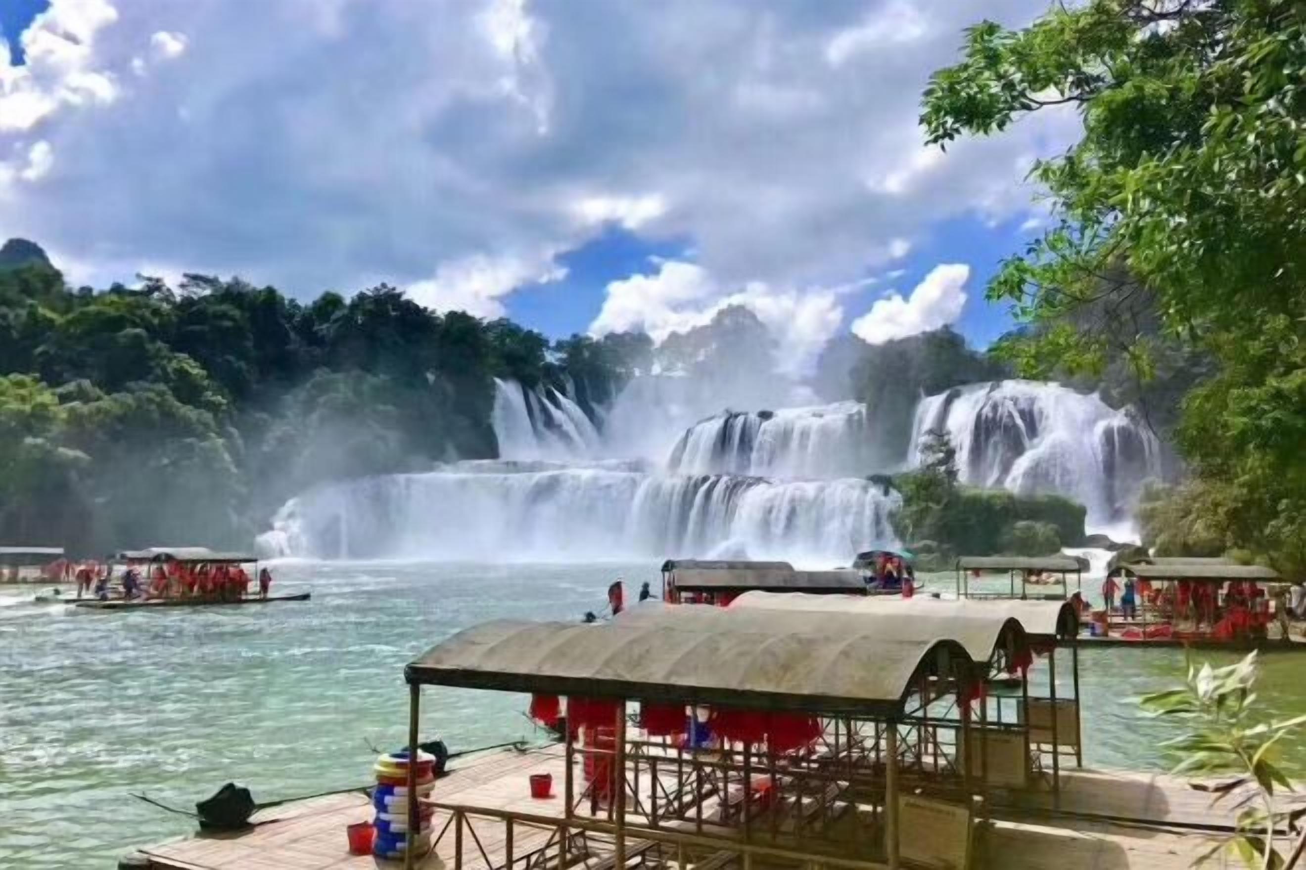 Ein Wasserfall, ein Steg mit Sitzgelegenheiten und ein bewaldetes Gebiet.